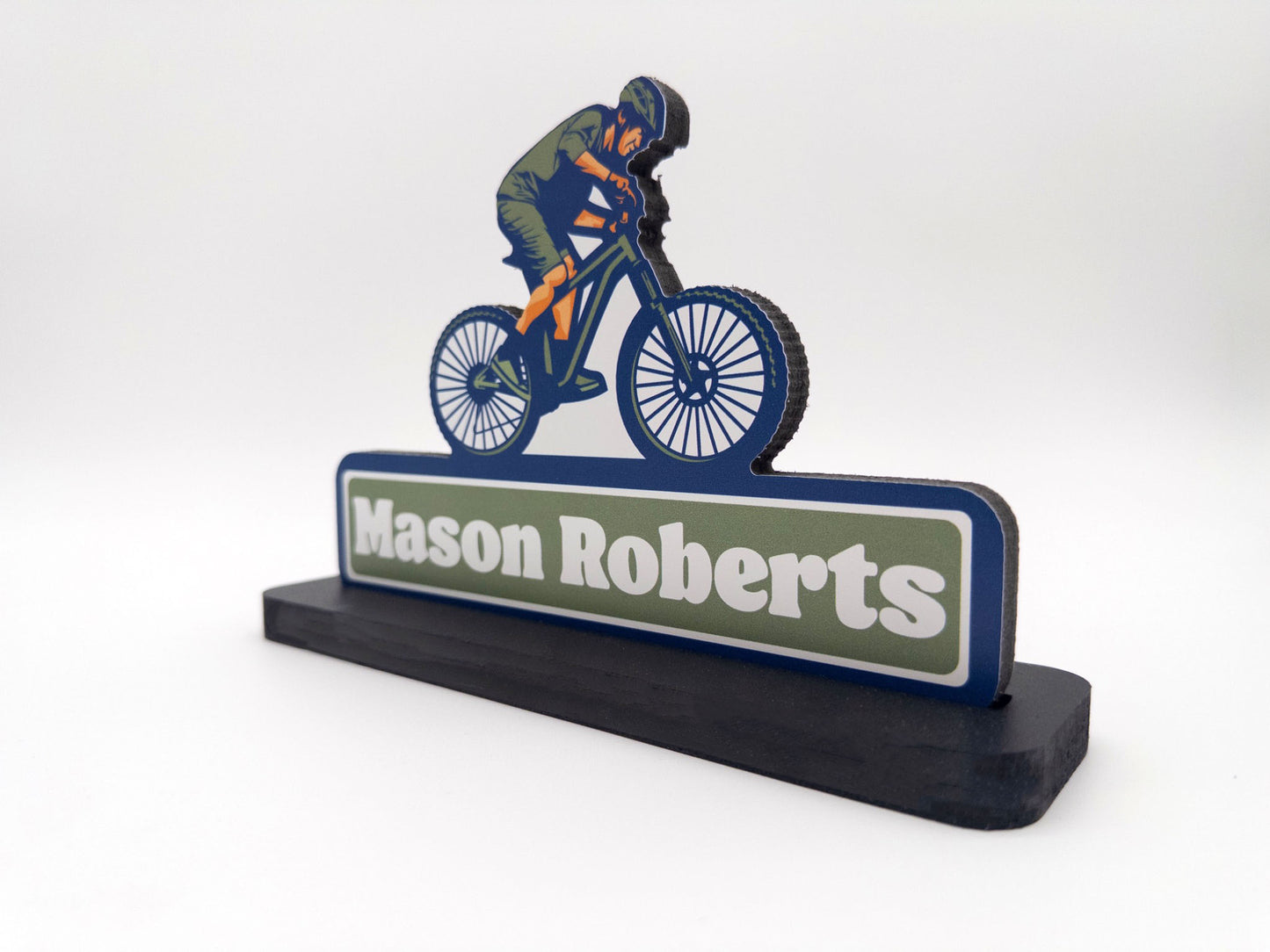 Angled side view of mountain biker desk sign with the name Mason Roberts against a white background.