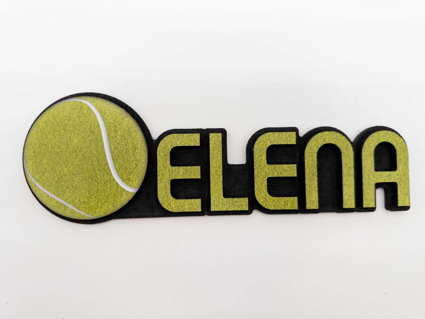 Overhead view of a personalized desk name plate with the name 'Elena' and a tennis ball design, ideal for a sports-themed workspace.