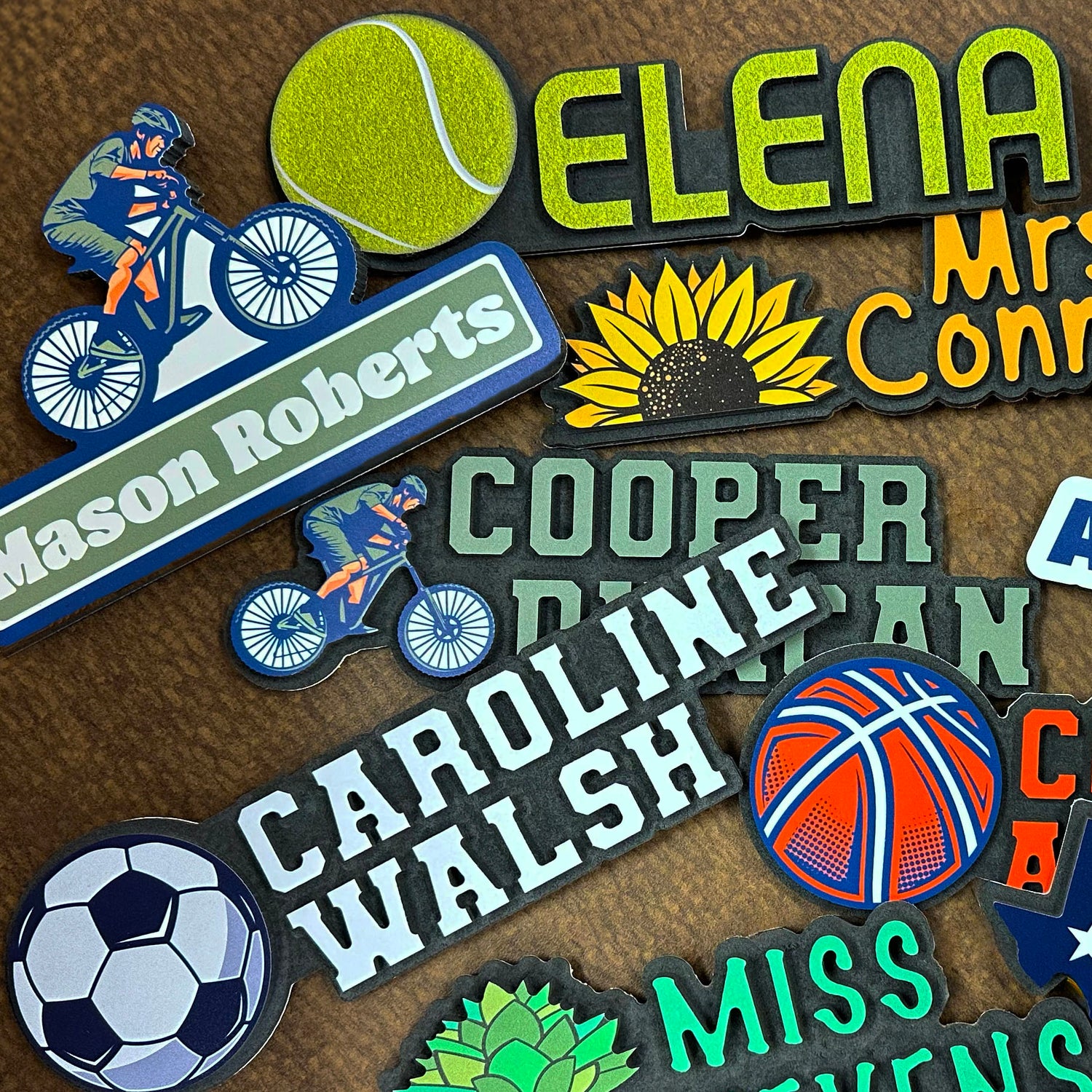 A collection of personalized name plates featuring various designs including sports, plants, and name themes on a brown background.