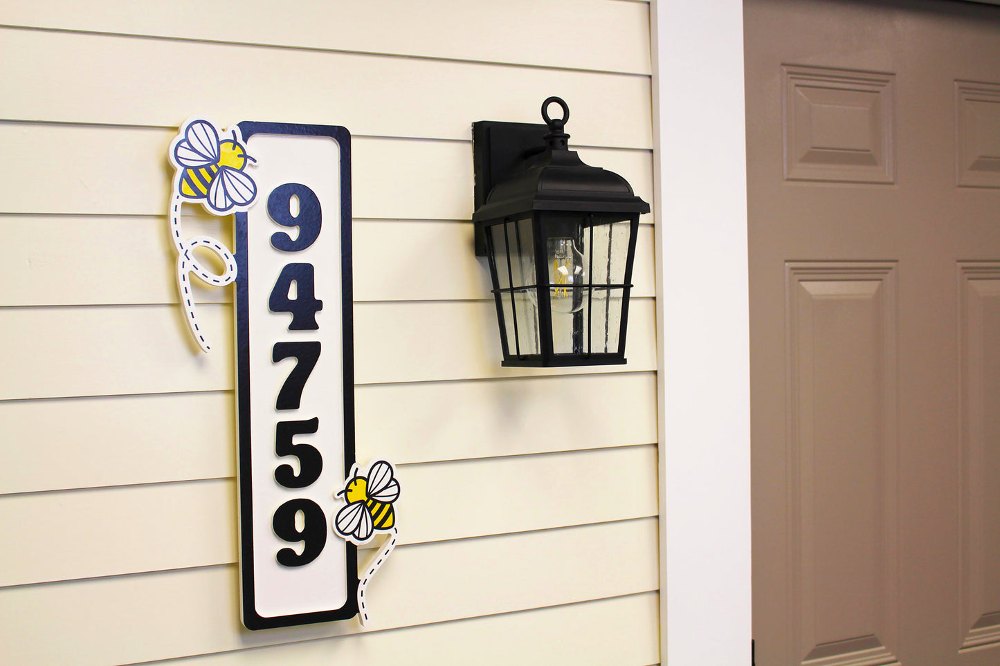 Angled view of a vertical house number sign with bee decorations near the top and bottom.