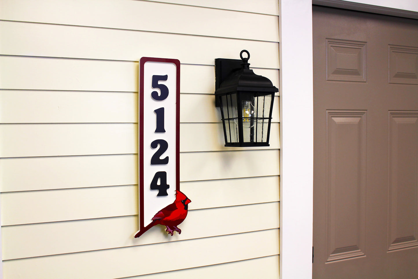 Angle view of a vertical house number sign with a red cardinal design mounted next to a door and black outdoor light.