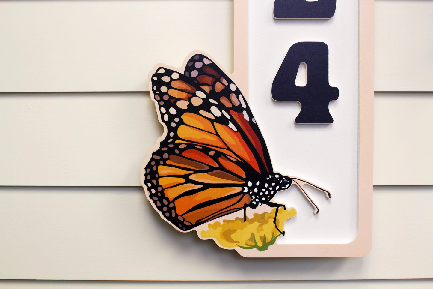 Close-up of a butterfly themed vertical house number sign.