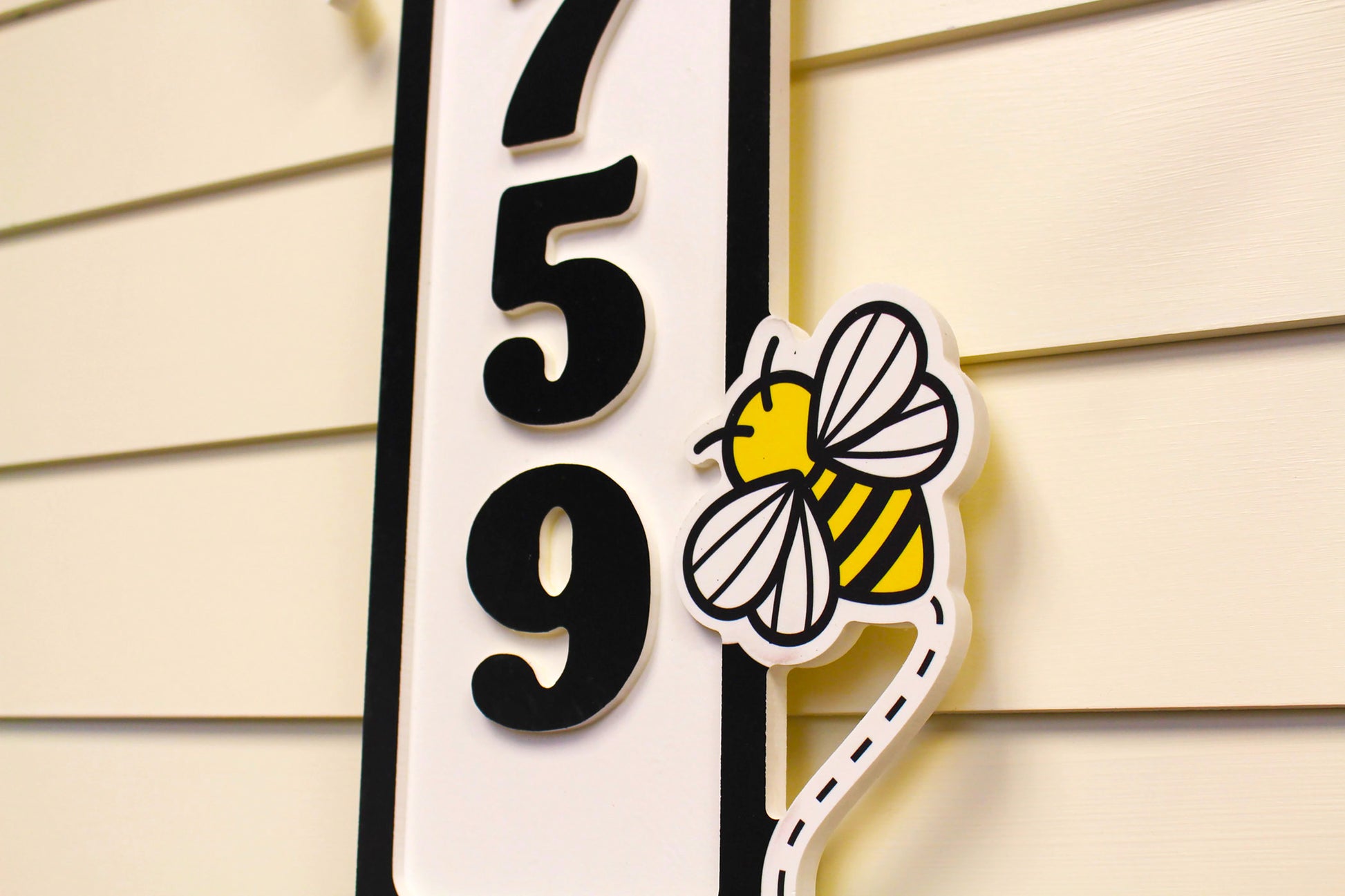 etailed view of a house number sign with bee decorations and raised black numbers.