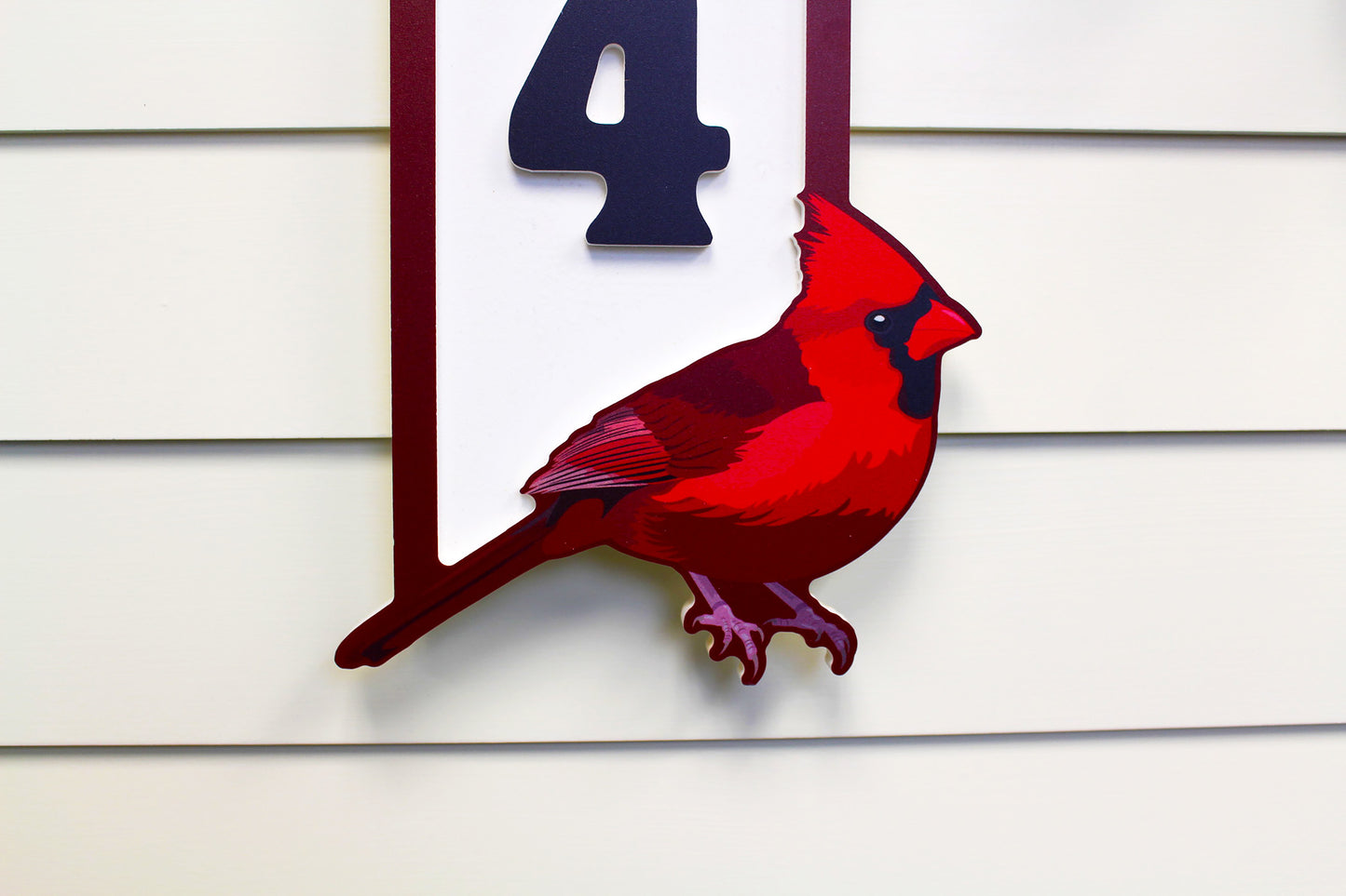 Close-up view of the top section of a house number sign featuring black numbers on a white background, with the cardinal visible at the bottom.