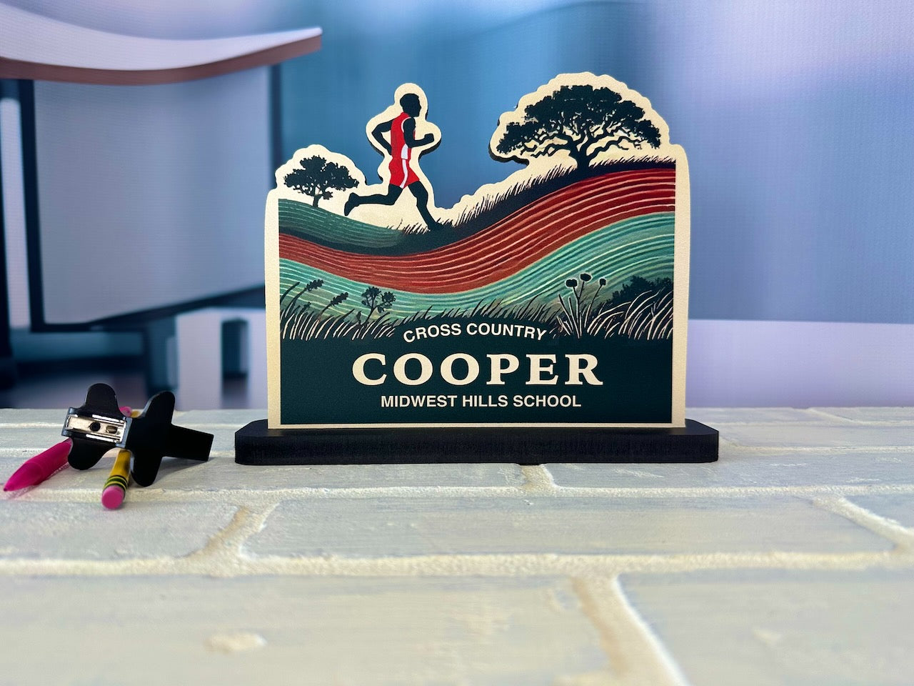 Cross country desk name plate showing male runner with scenic hills and tree background, labeled Cooper - Midwest Hills School.