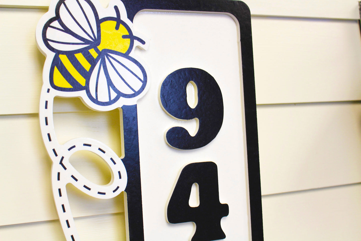 Close-up detailed view of house number sign with a bee decoration and raised numbers.