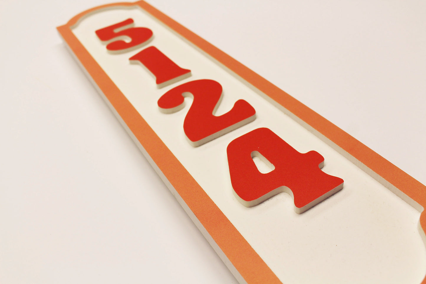 Flat lay of orange border house number sign with raised numbers.