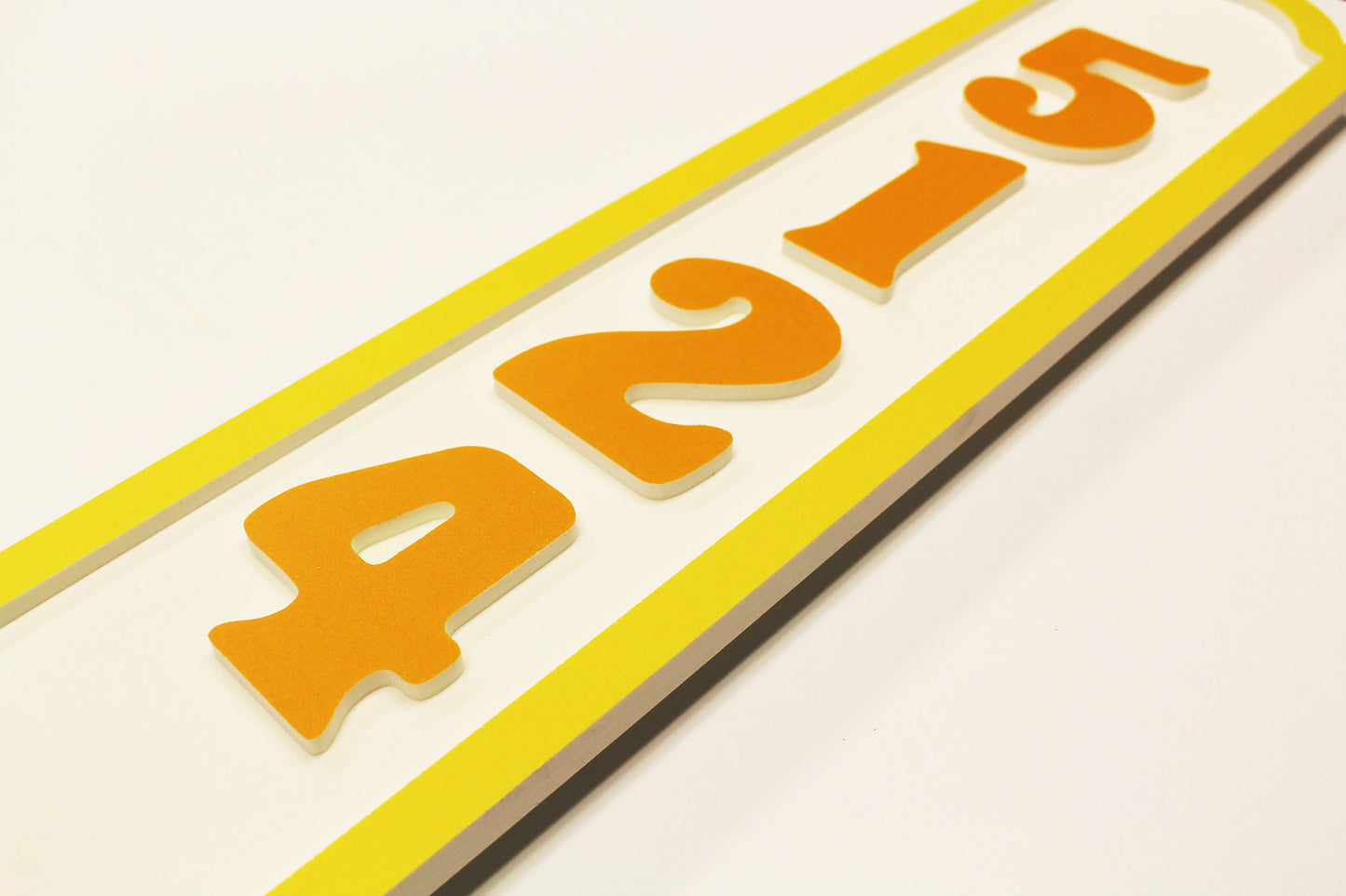 Flat lay of a yellow border house number sign with raised numbers.