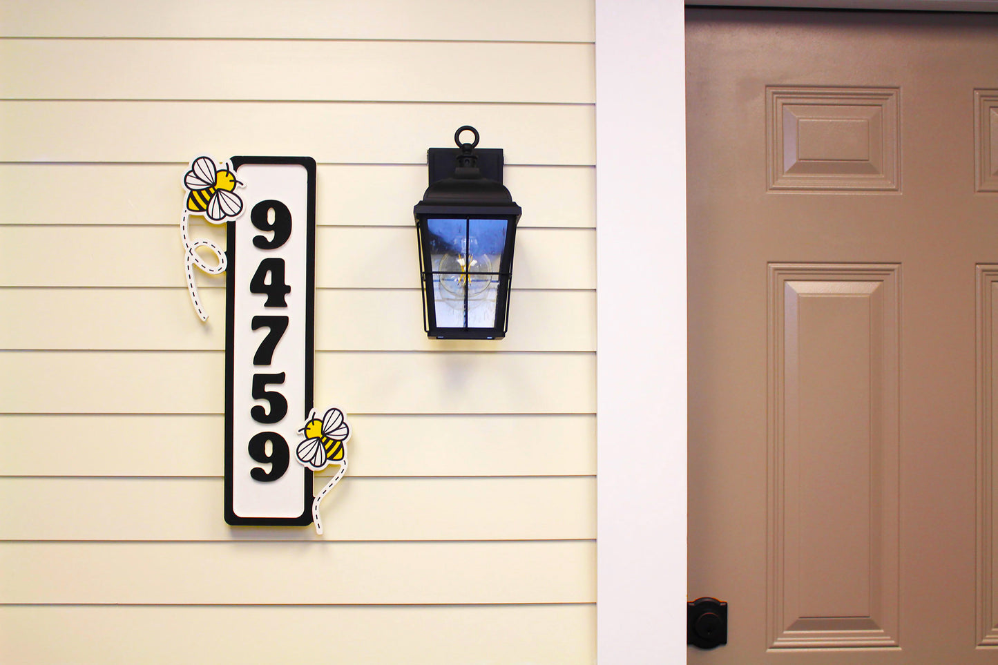 Full front view of a house number sign with two bee decorations, displayed near a front door.