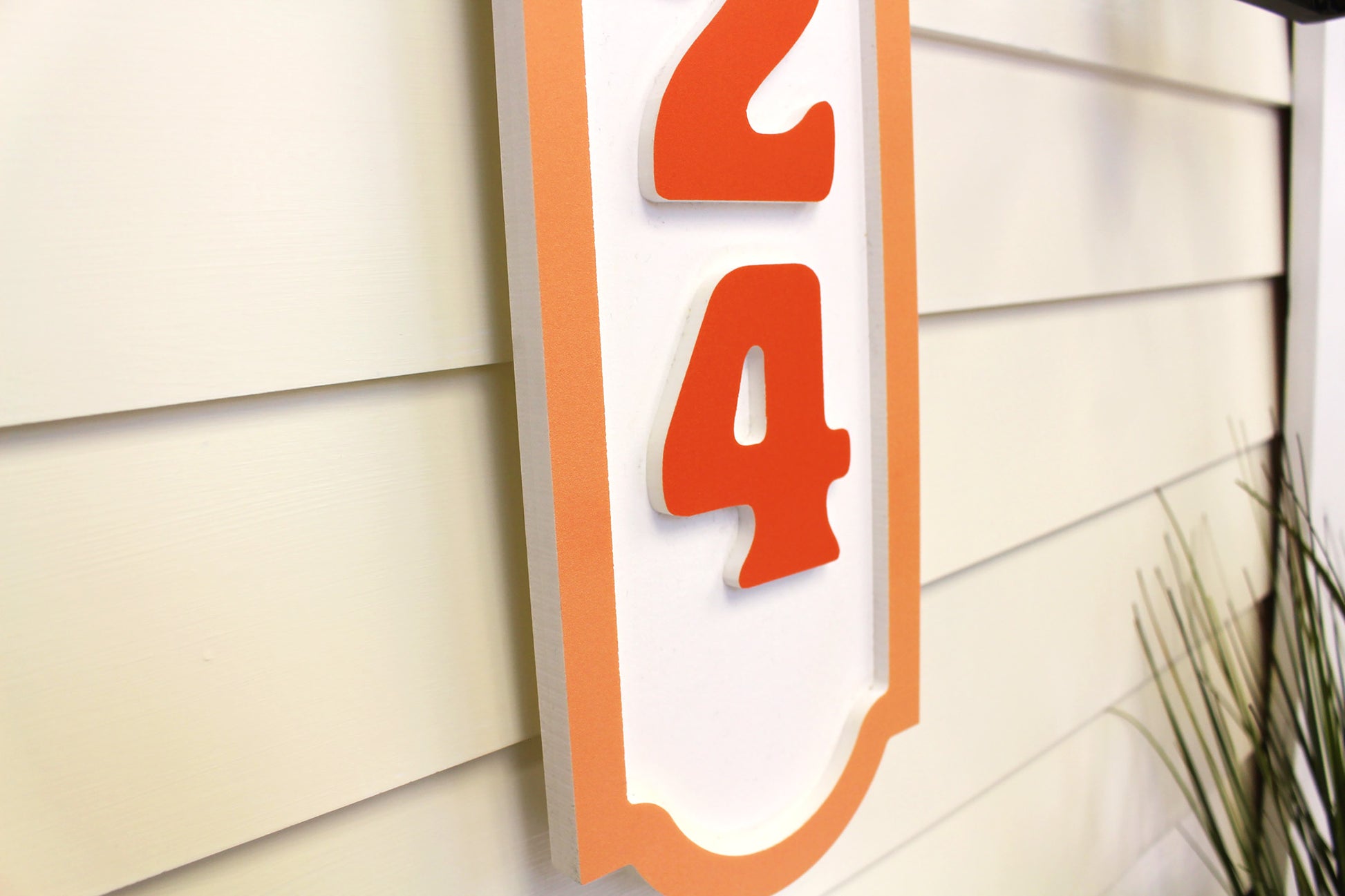 Close-up view of an orange-bordered house number sign with raised orange numbers, highlighting the details and texture.