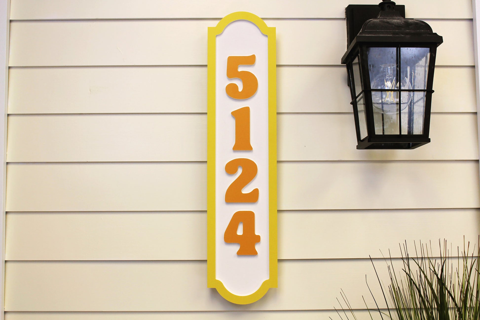  Vertical house number sign with yellow border and orange numbers, displayed near an outdoor light fixture.