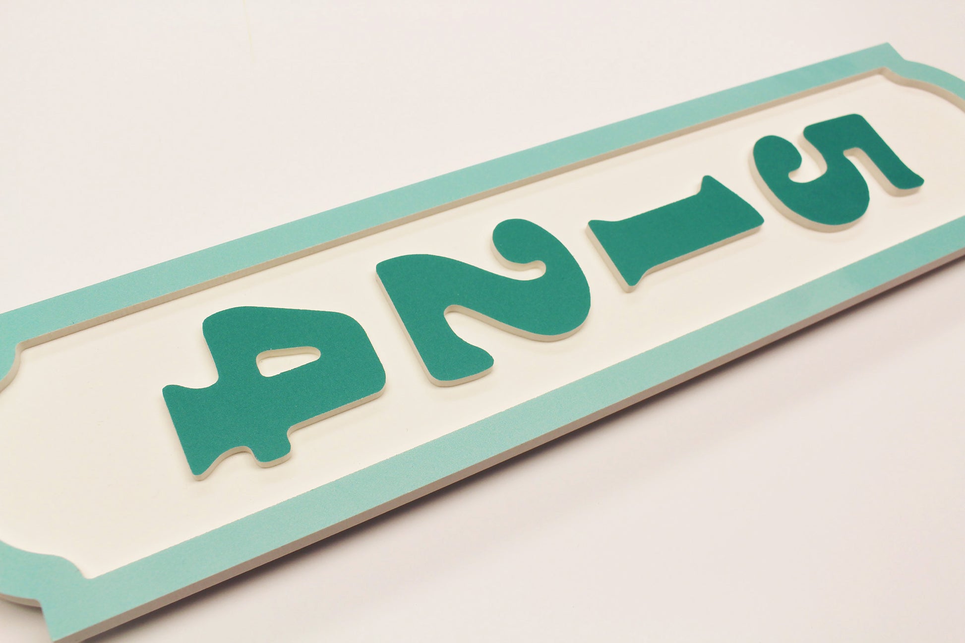 Flat lay of teal house number sign showing raised number cutouts.