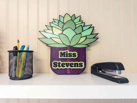 Succulent room sign labeled 'Miss Stevens' placed on a shelf.