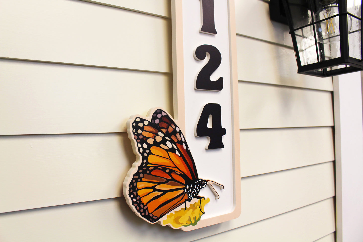 Side view of a vertical house number sign with a butterfly, highlighting the 3D effect.