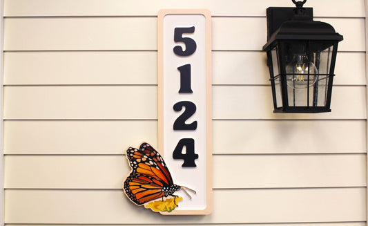 Vertical house number sign with a butterfly design mounted next to a lantern.